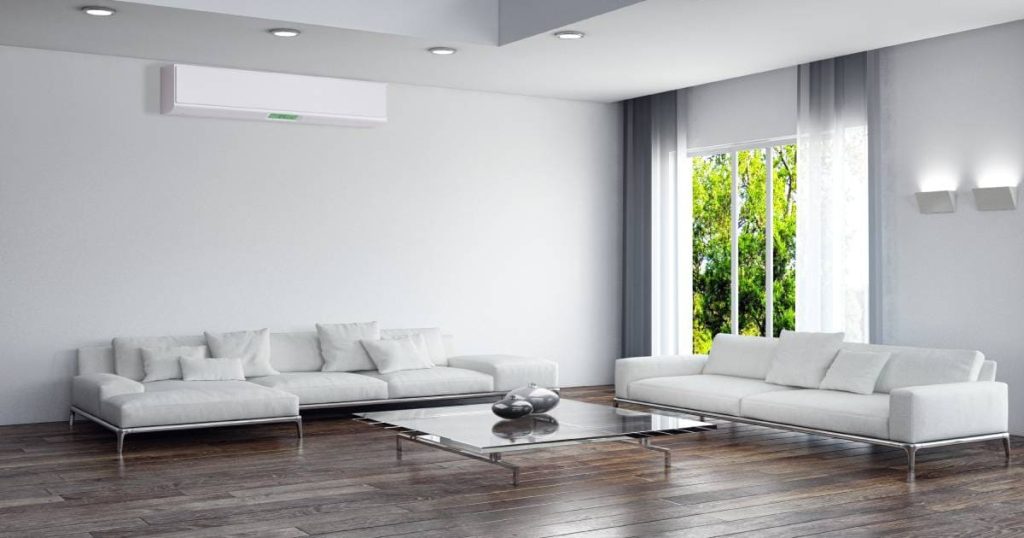 Een witte split-airco unit in een ruime moderne woonkamer. De kamer heeft een houten vloer en een raam met uitzicht op de tuin. 