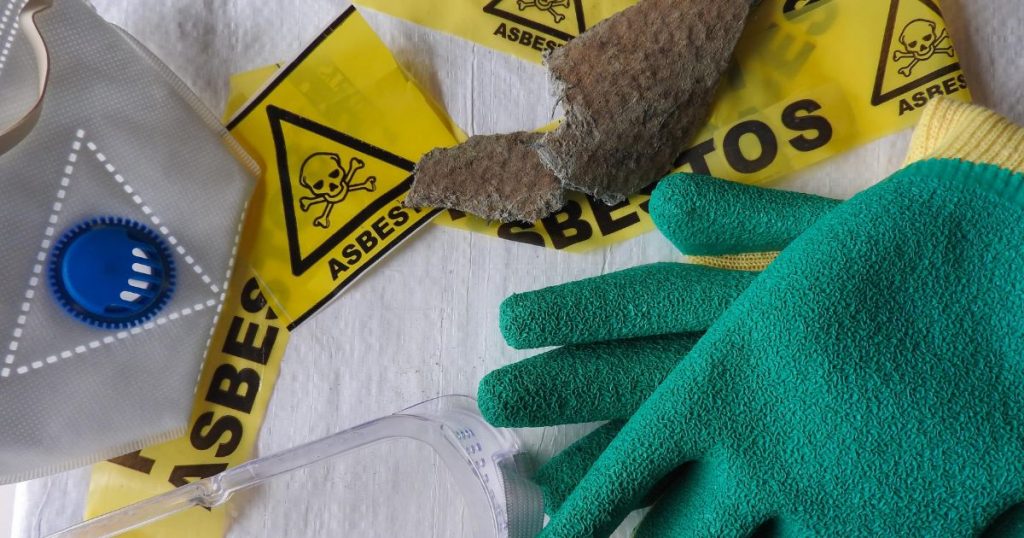 Een witte ondergrond met daarop beschermende asbest handschoenen, een masker, asbestlint en een stuk asbest. 