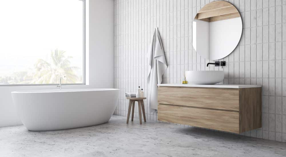 Een badkamer met een vloer van beton ciré, een losstaand wit bad en een houten wastafel. 