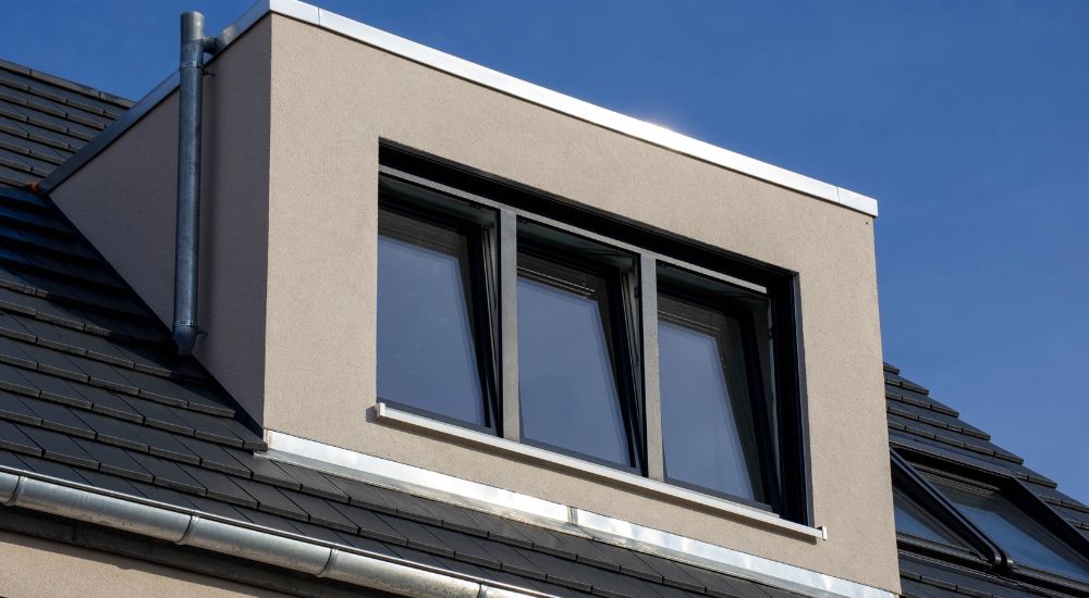 Dakkapel op een hellend dak met zwarte leien. De dakkapel zelf is afgewerkt in crepi. Ernaast zijn ook nog 2 Veluxramen geïntegreerd in het dak.