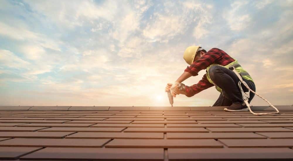 Een dakwerker met gele helm en houthakkershemd legt de laatste hand aan een leien dak.