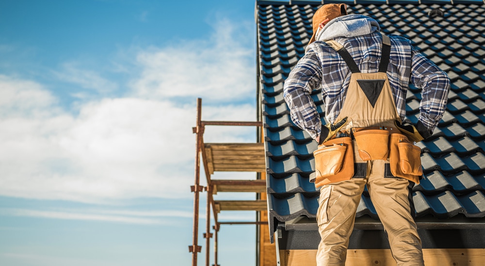 Een dakwerker kijkt met de armen in de zij vanop een stelling naar het afgewerkte hellend dak.