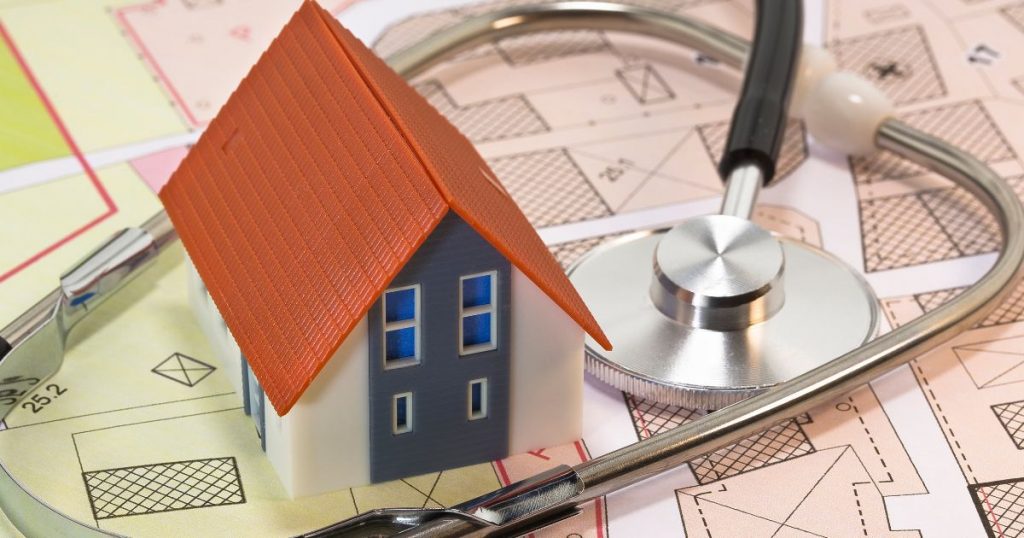 Een klein speelgoedhuisje met daaromheen een stethoscoop op een ondergrond met bouwtekeningen. 