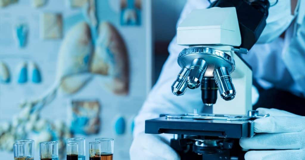 Een onderzoeker kijkt door een microscoop naar een asbestmonster. 