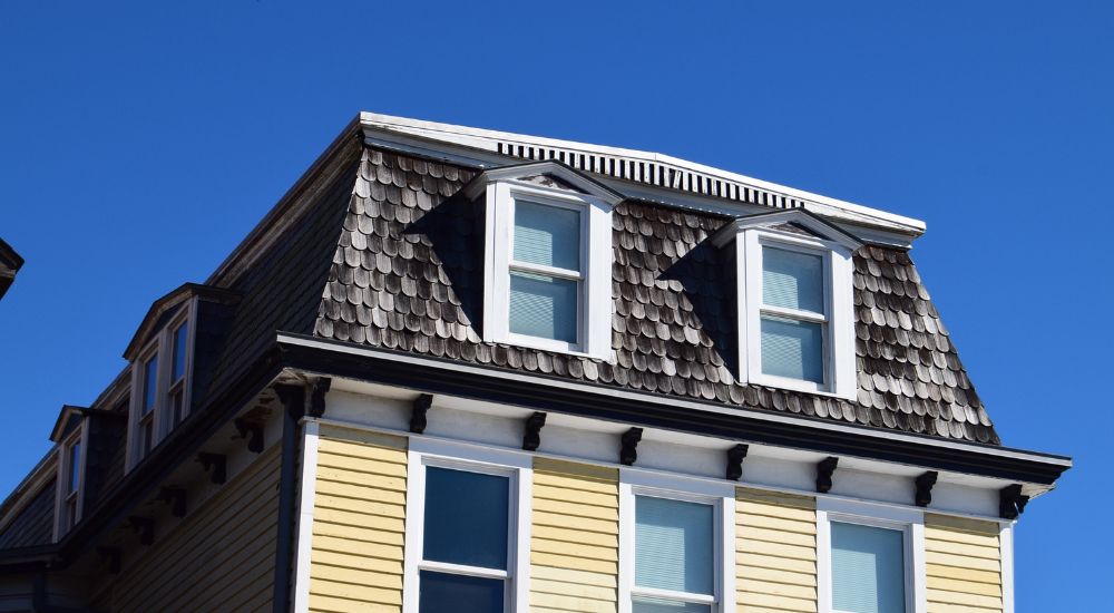 Klassiek mansardedak met witte ramen bovenop een woning  met lichtgele gevelplaten in rabat.