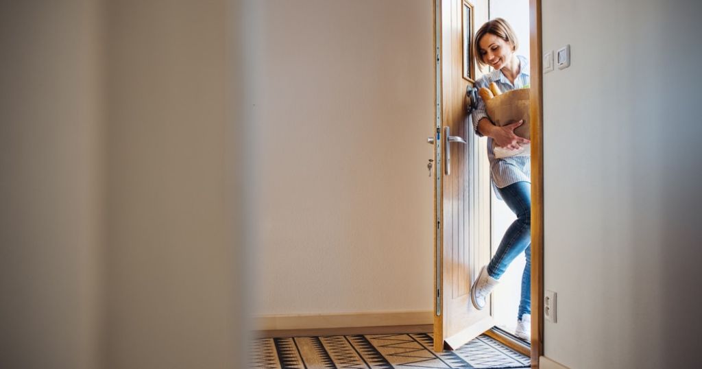 Een nieuwe voordeur met een veilig slot. Een vrouw komt binnen met boodschappen in haar handen.