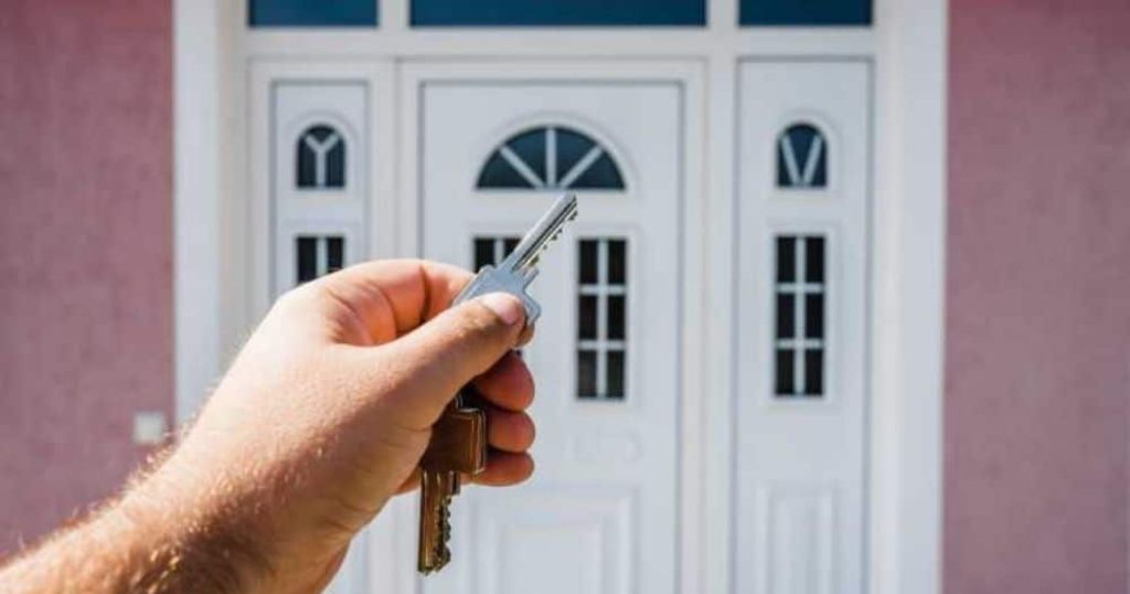 Een klassieke, witte voordeur in kunststof: op de voorgrond toont een hand de sleutel van de deur.