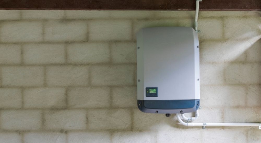 Een witte thuisaccu met donkergrijze rand, gemonteerd aan een witte bakstenen muur.