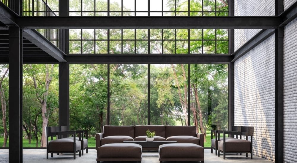 De hoge stalen ramen brengen heel wat natuurlijk licht naar binnen in het sobere, donkere interieur van de woning.