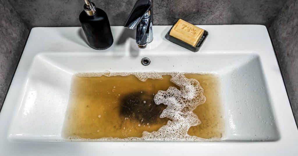 Een witte gootsteen in een grijze keuken met een stinkende, verstopte afvoer.