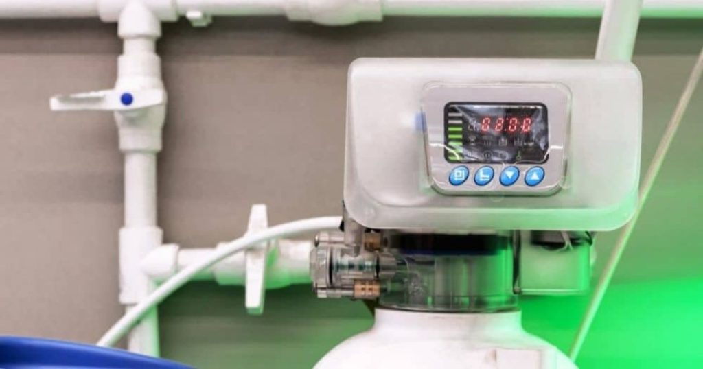 Een display van een waterontharder tegen een grijze muur met witte leidingen. 