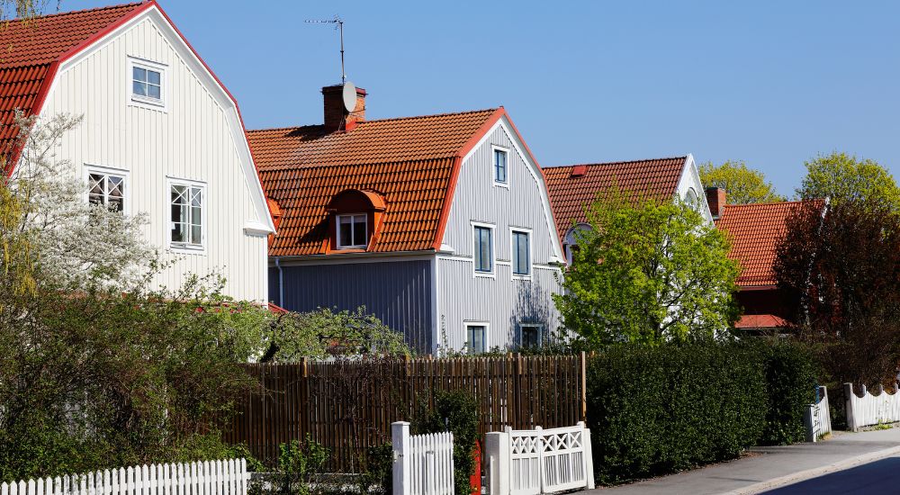 2 houten woningen naast elkaar met een mansardedak met rode dakpannen.