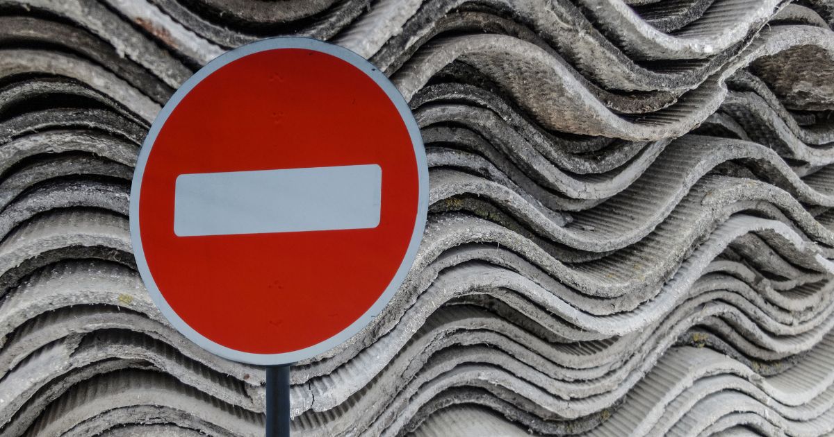 Een rood met wit "verboden" bord voor een stapel golfplaten van asbest. 