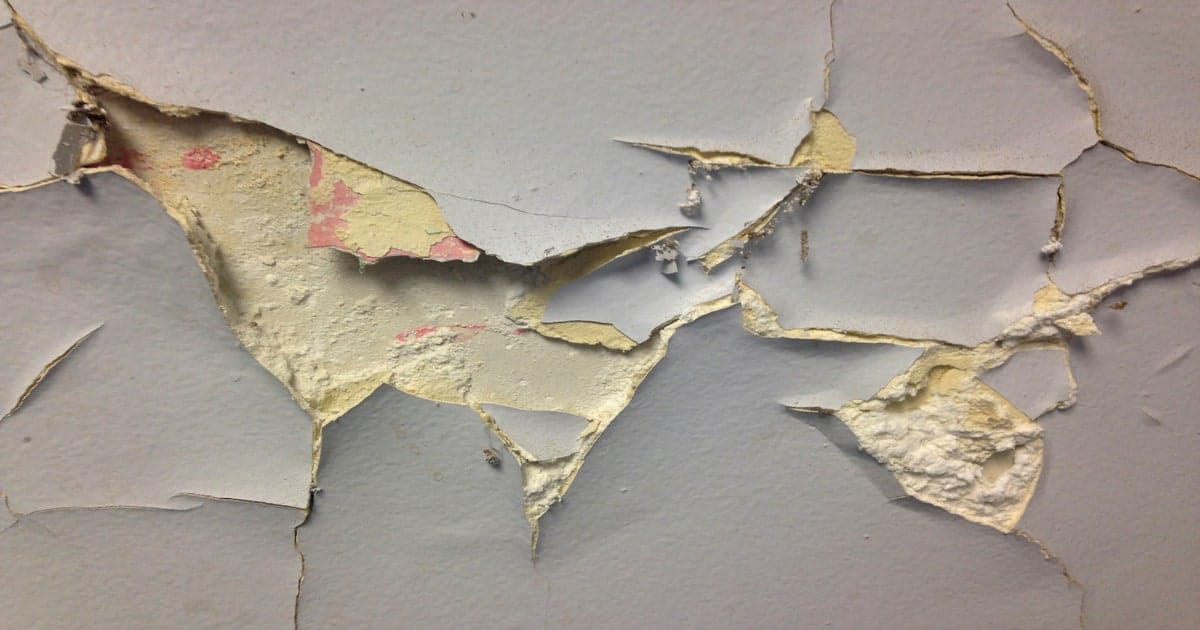 Beschadigde muur met asbestlijm eronder