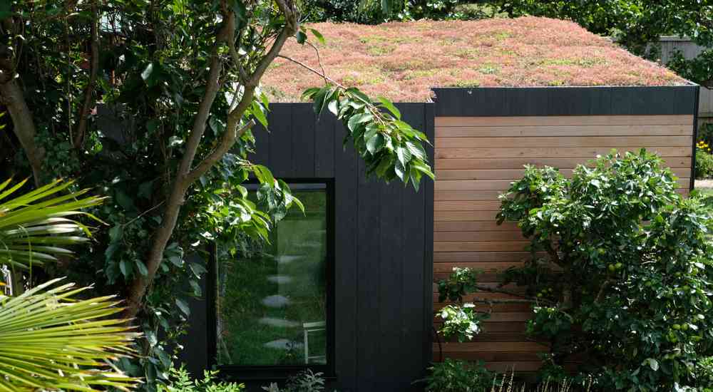 Modern tuinkantoor met extensief groendak van rood-groen kleurige mossen en vetplanten.