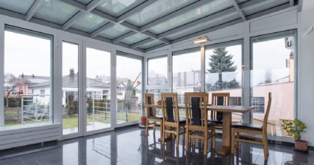 Een glazen serre waar condens geen probleem is: de veranda is voorzien van dubbel glas, mechanische ventilatie, aluminium profielen met thermische onderbreking en een geïsoleerde vloer. In de serre staan een houten tafel en zes stoelen.