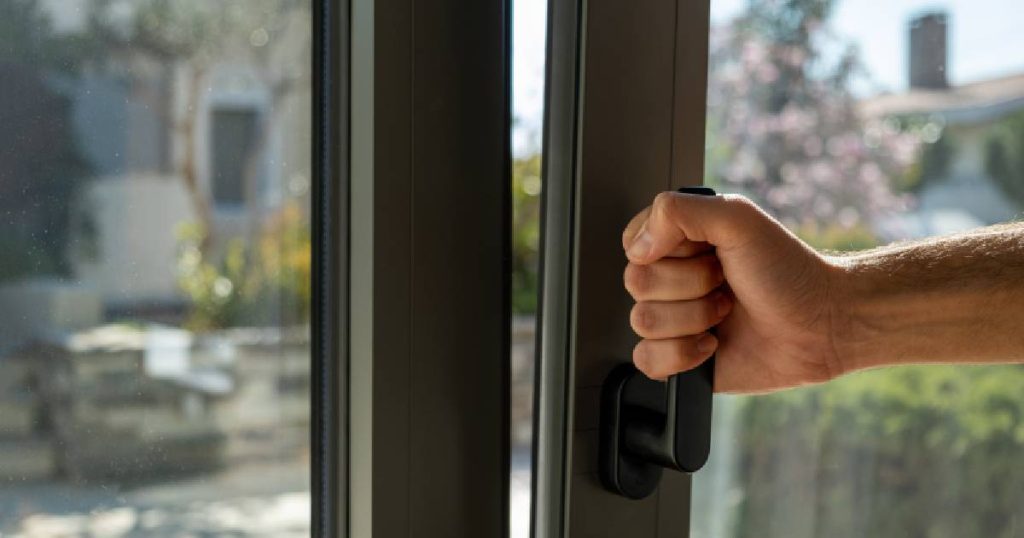 Een mannenhand opent het raam in een serre om condens te voorkomen.