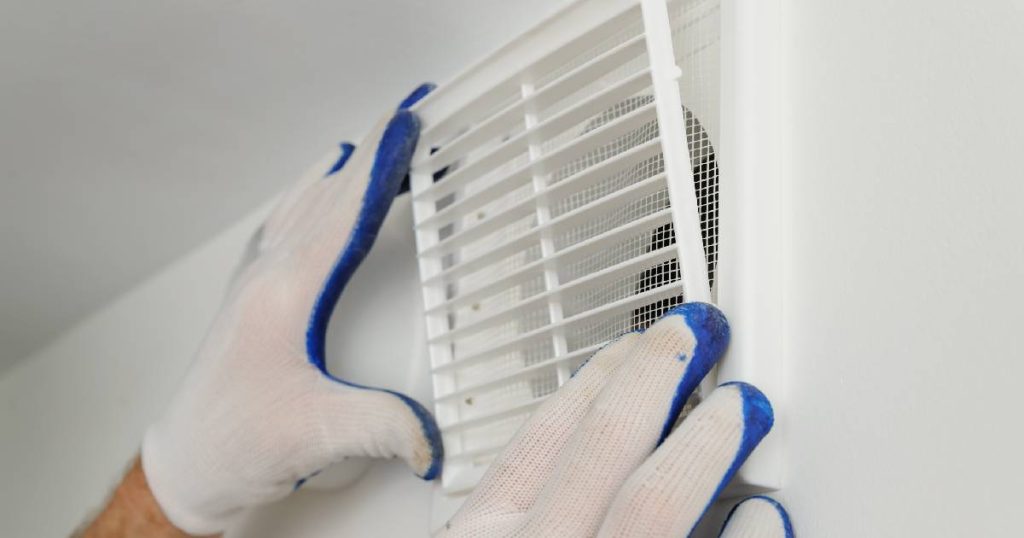 De handen van een serrespecialist in wit met blauwe werkhandschoenen plaatsen een ventilatierooster in een serre om condens te voorkomen.