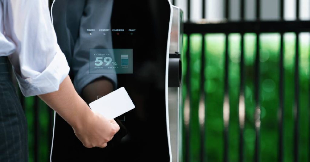 Een dame in wit hemd gebruikt haar laadpas om haar eigen laadpaal, die ze openbaar liet maken, te gebruiken om haar elektrische auto op te laden.