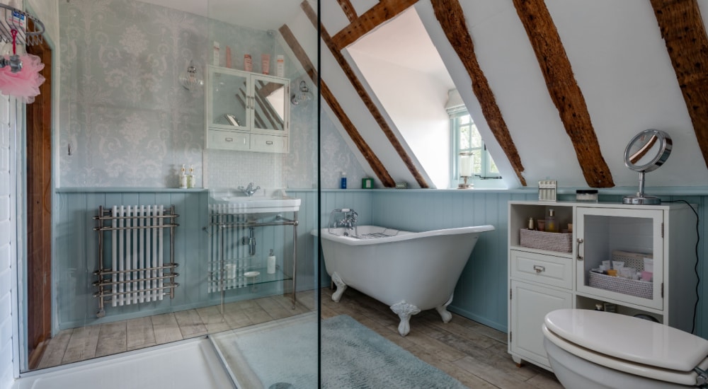 Een vrijstaand gietijzeren bad in de hoek van een badkamer met een schuin dak en blauwe details.