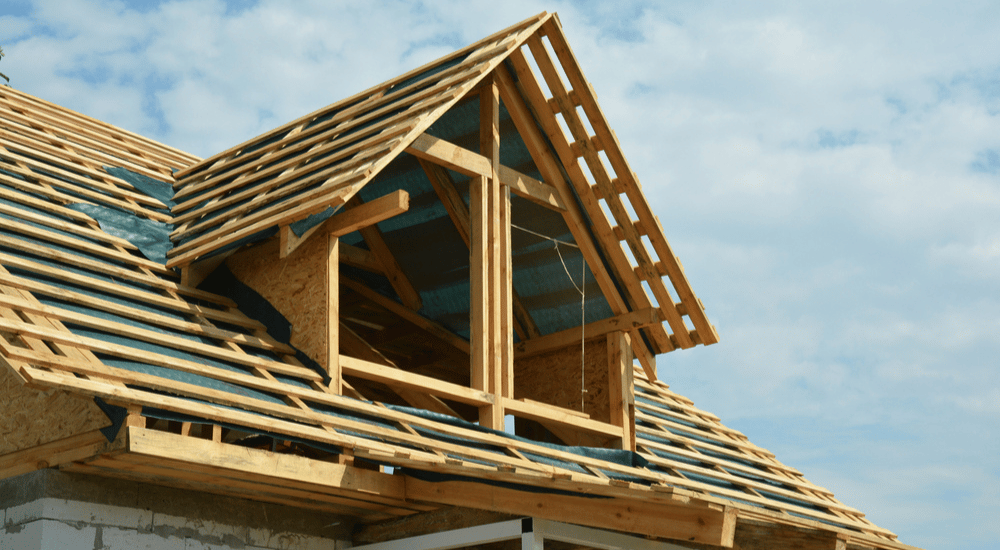 Een houten gordingen dak tegen een blauw bewolkte lucht. 