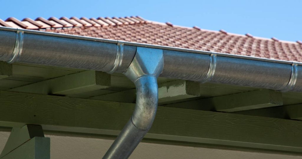 Een zinken hanggoot tegen een groene gevelbalk onder een pannendak.