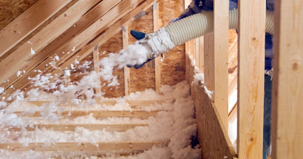 Hoe is men deze zolder aan het isoleren? Een isolatiespecialist spuit losse isolatie tussen de houten vloerbalken.