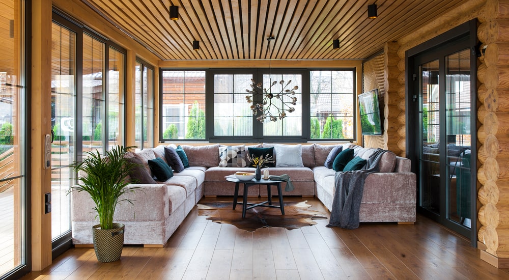 Serre van hout met veel ramen en een grote bank erin. aan de muur hangt een televisie en in het midden staat een kleine tafel op een kleed