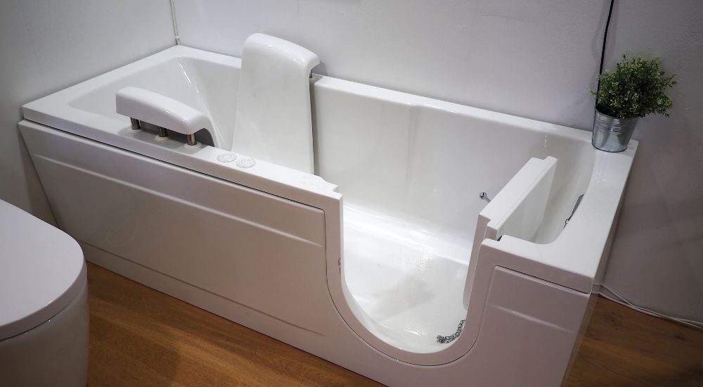 Een wit bad met een instapdeur om te voorkomen dat je uitglijdt. Het bad staat op een houten vloer. 