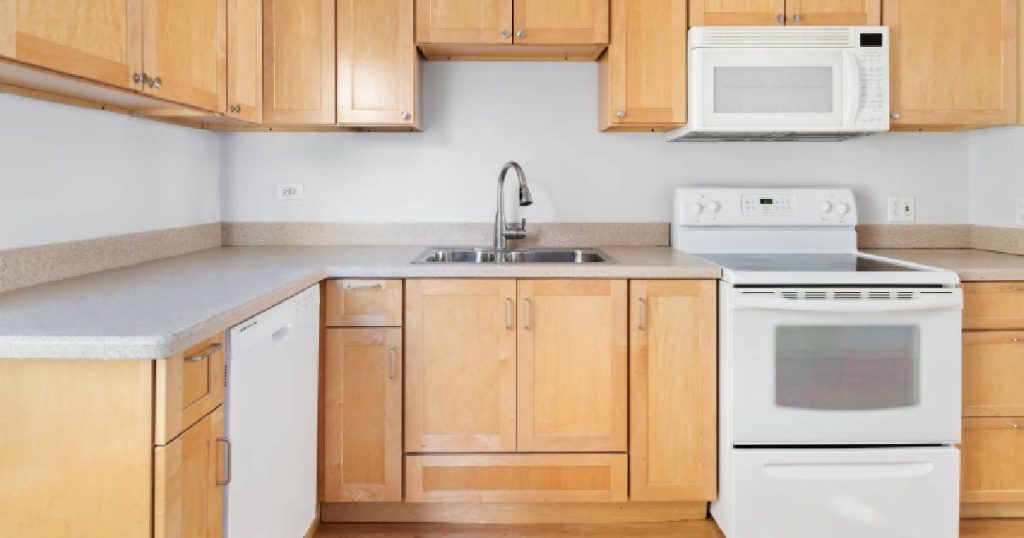 Een eenvoudige keuken, goedkoper dan de gemiddelde prijs voor een keuken, met eenvoudig fornuis, ingebouwde magnetron, vaatwasser en kasten uit kunststof met houtlook.