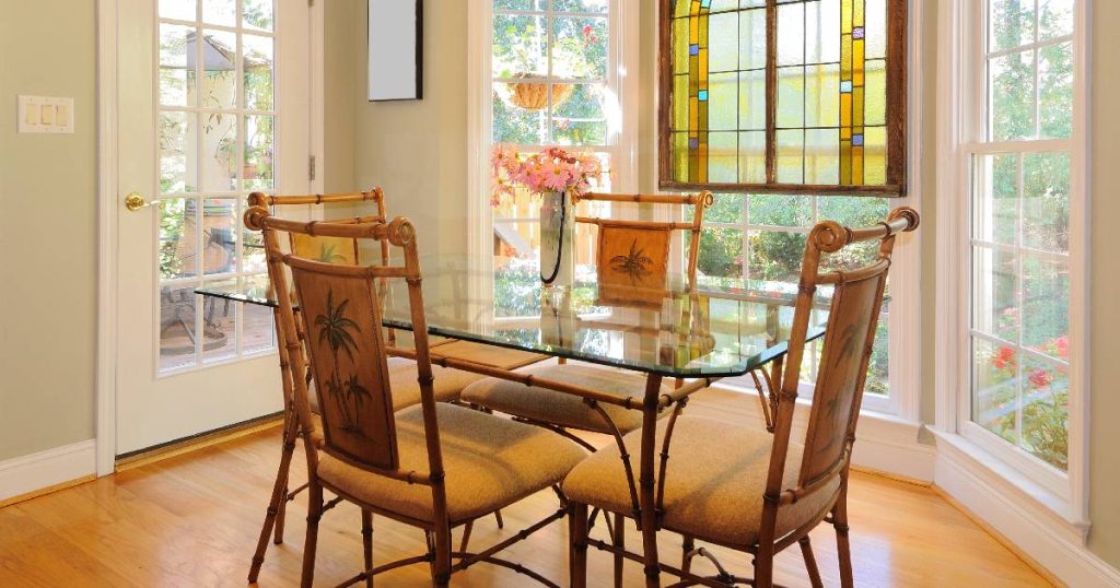 Een uitbouw met grote glazen ramen van een oude keuken dient als eethoek.