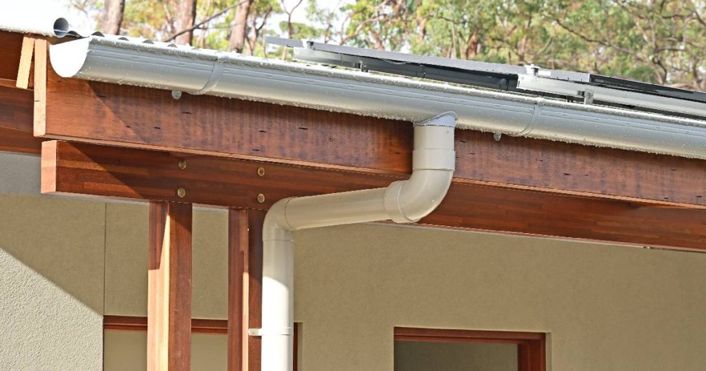 Een klassieke, halfronde dakgoot of hangoot in wit kunststof, bevestigd aan een houten gevelbalk.