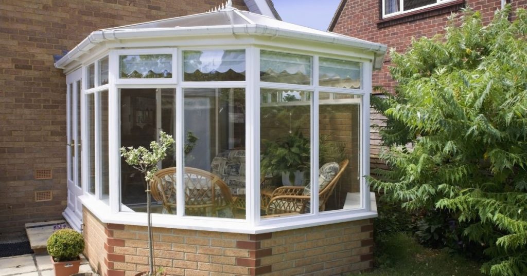 Witte houten serre in de achtertuin aan het huis gebouwd. In de serre zijn stoelen te zien