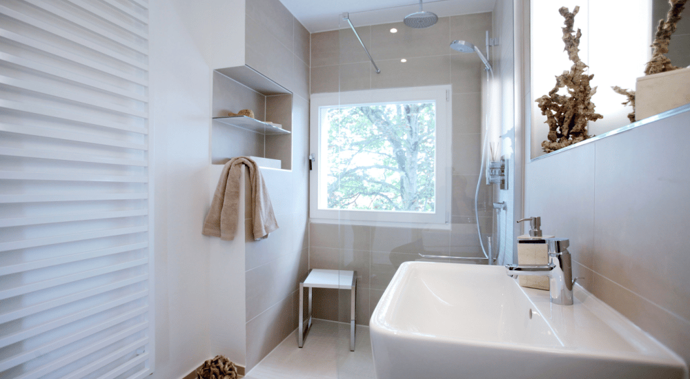 Een kleine badkamer met licht gekleurde tegels en een glazen douchewand om de ruimte optisch te vergroten. 