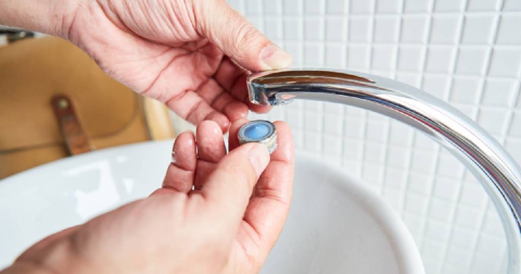 Twee handen draaien de perlator (ook wel de filter of het zeefje) van een vaste kraan los. Een belangrijke stap in het ontkalken van een kraan.