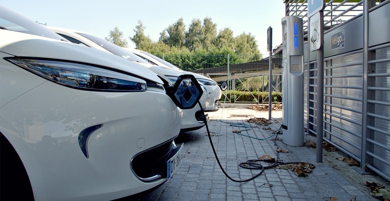 Drie witte elektrische wagens aan een elektrische laadpaal, verbonden met losse laadkabels.