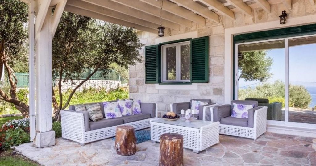 Houten landelijke overkapping met open zijkanten. In de serre staan tuinmeubels met kussens erop.