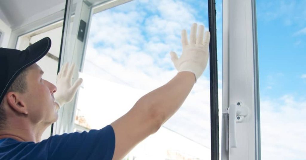 Een installateur plaatst behoedzaam het vensterglas in de nieuwe kunststof raamprofielen.