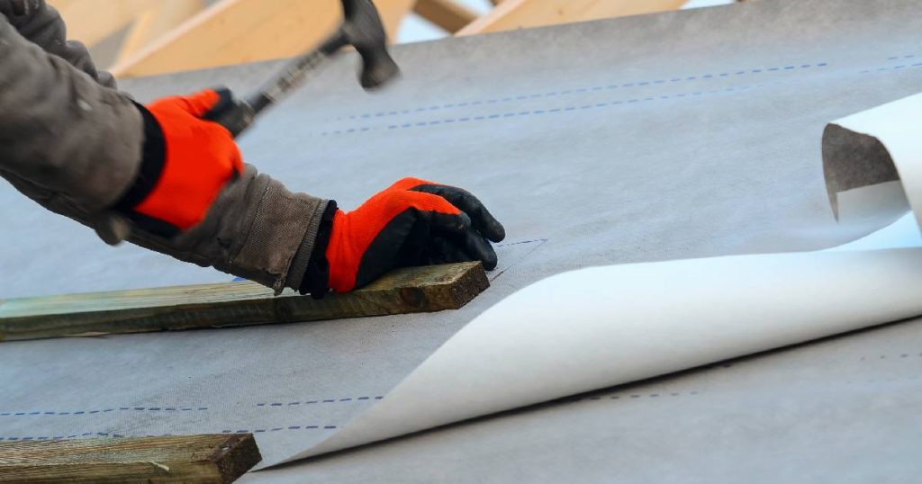 Een dakwerker plaatst een onderdak met onderdakfolie op de dakconstructie.