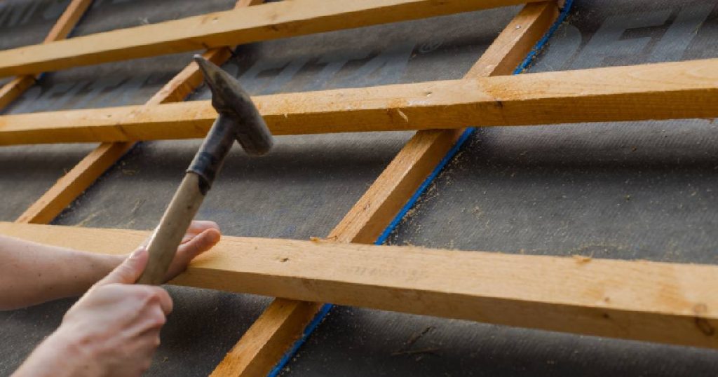 Een dakwerker bevestigt de pannenlatten op de tengellatten, die op hun beurt bevestigd zijn op het onderdak.