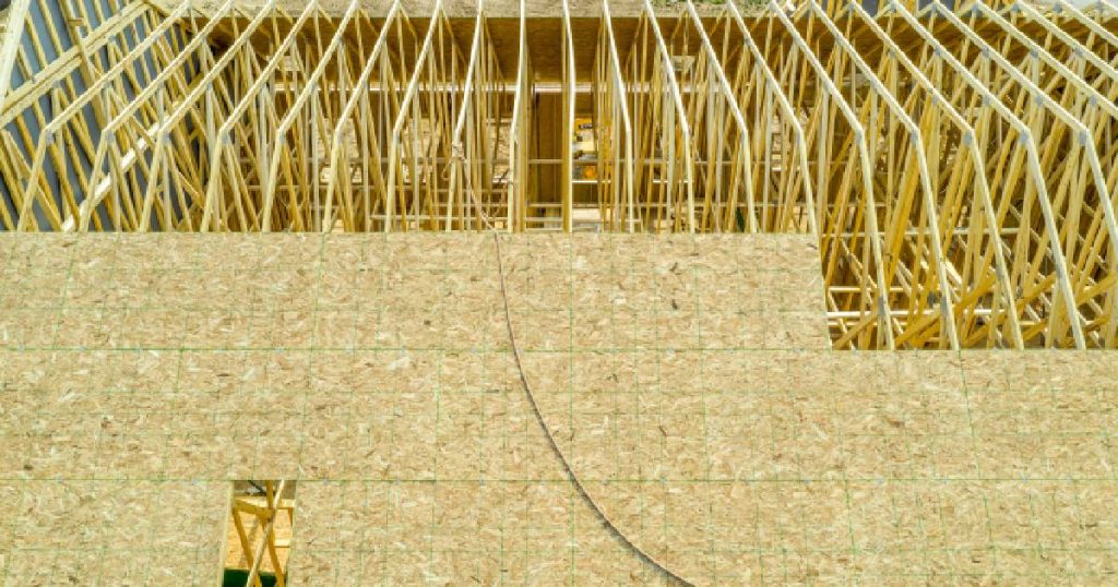 Het dak van een nieuwbouwwoning wordt bedekt met een onderdak van houtvezelplaten. Het dak is nog niet geïsoleerd: de spanten zijn nog zichtbaar.