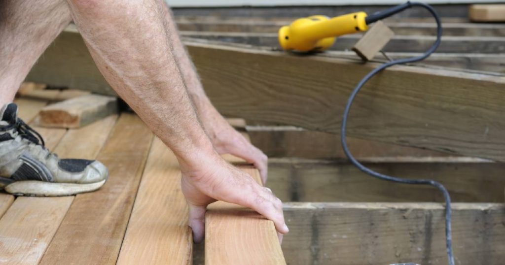 Een man is bezig met het renoveren van de fundering en vloer van een oude houten serre.