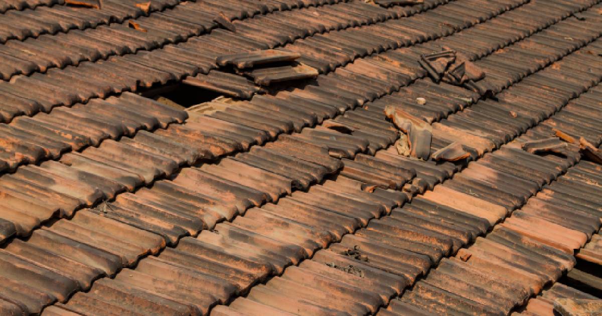 Oude betonnen dakpannen op een hellend dak. De dakpannen zijn oud en versleten.