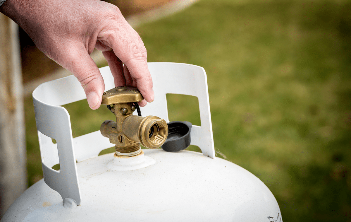 een hand draait aan de kraan bovenop een witte propaantank