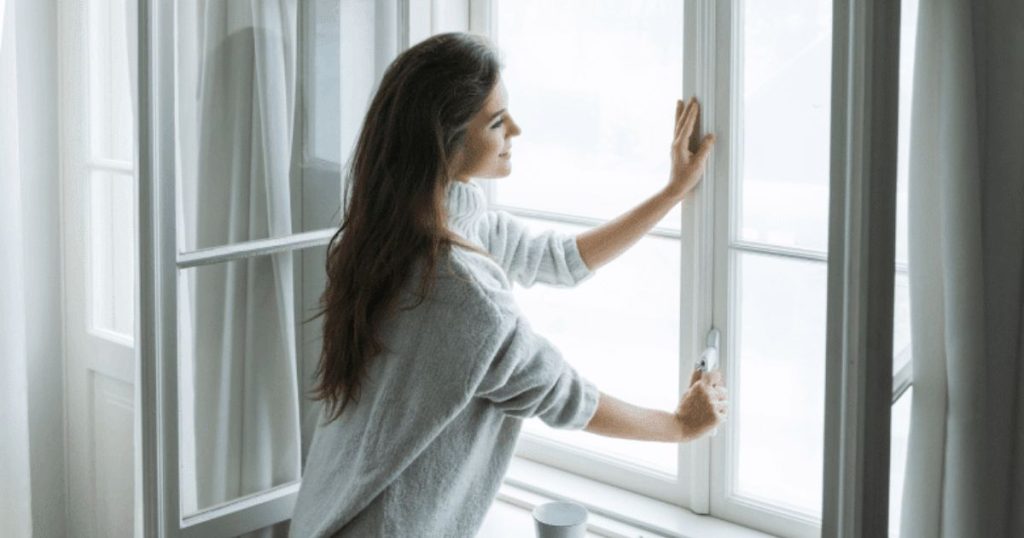 Een jongedame met donkerbruine haren en wollen trui sluit de witte kunststof kozijnen in haar woning. De binnenramen, ook in kunststof, laat ze openstaan. Of is ze ook van plan die te sluiten?