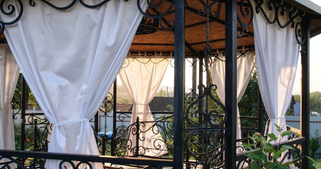 Een zwarte, smeedijzeren serre, afgesloten met witte doeken.