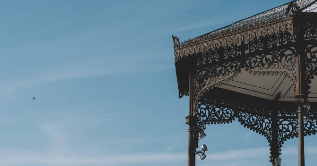 Het dak van een smeedijzeren serre, afgewerkt met complexe, krullende en ronde vormen.