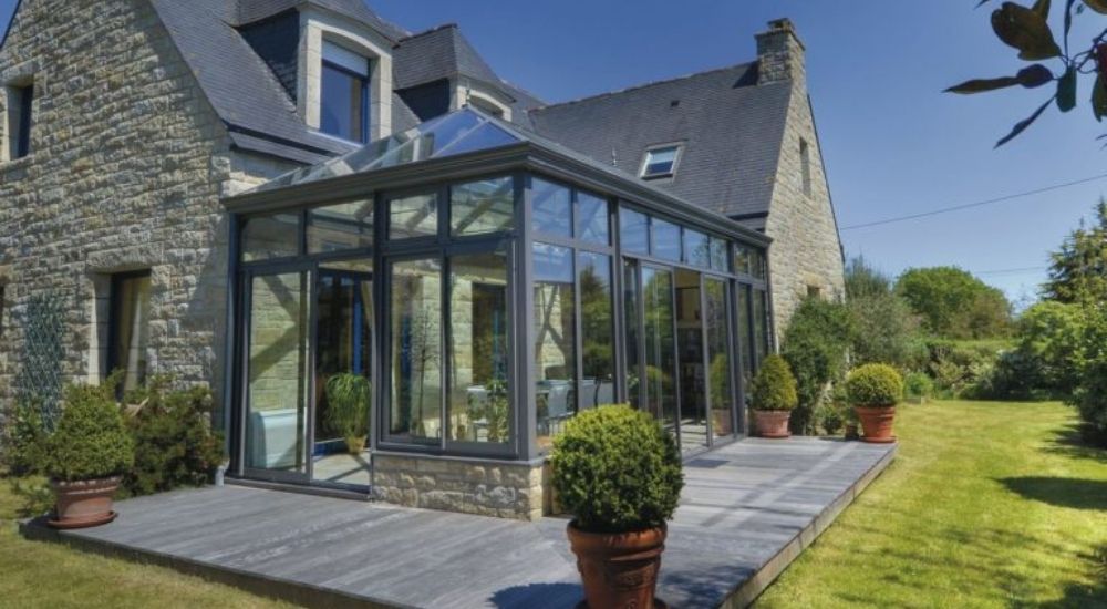 Een glazen serre aan een huis. Bij de serre zijn glazen schuifdeuren aangebracht.