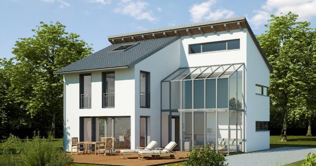 Een ruime witte woning met een grote stalen serre met 2 verdiepingen en smalle, grijze profielen. Voor de serre ligt een houten dek met zonnestoelen en een houten tafel met stoeltjes.