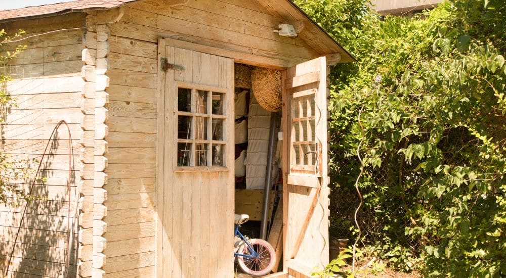 Een houten tuinhuis wordt gelucht met een open deur voor ventilatie.